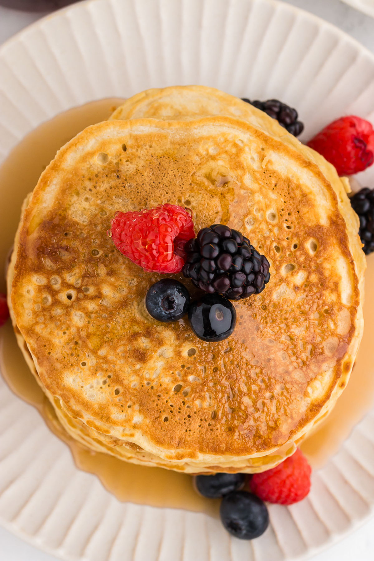 top view of golden dairy free buttermilk pancakes with syrup and berries on a white plate