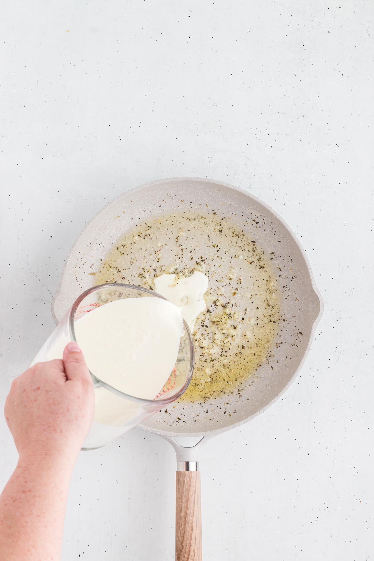 pouring hte cream into the garlic for homemade alfredo sauce