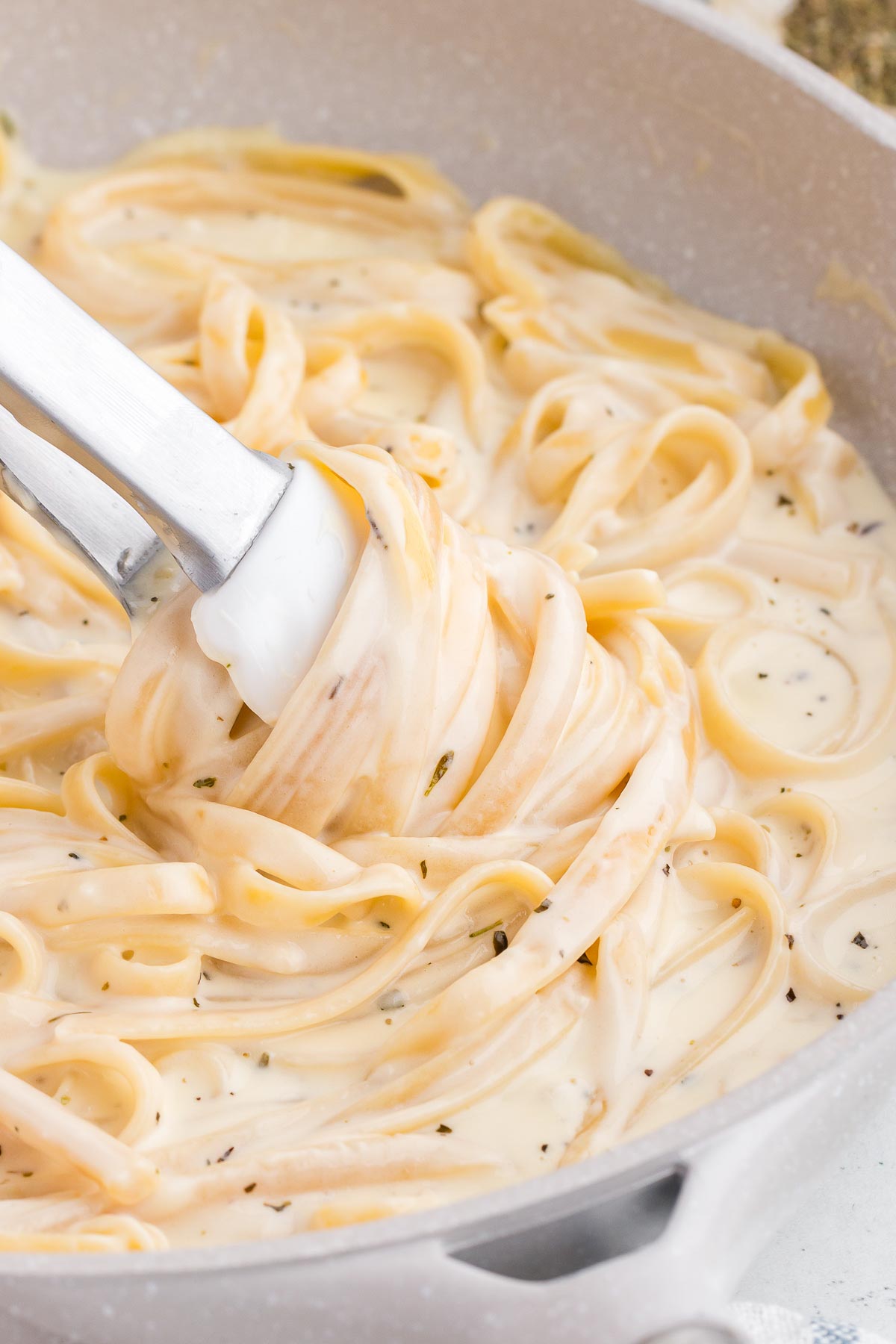 tongs tossing fettucine in homemade alfredo sauce