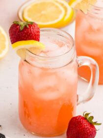 mason jar style mug full of Easy Strawberry Lemonade with strawbrerries and lemon slices around it