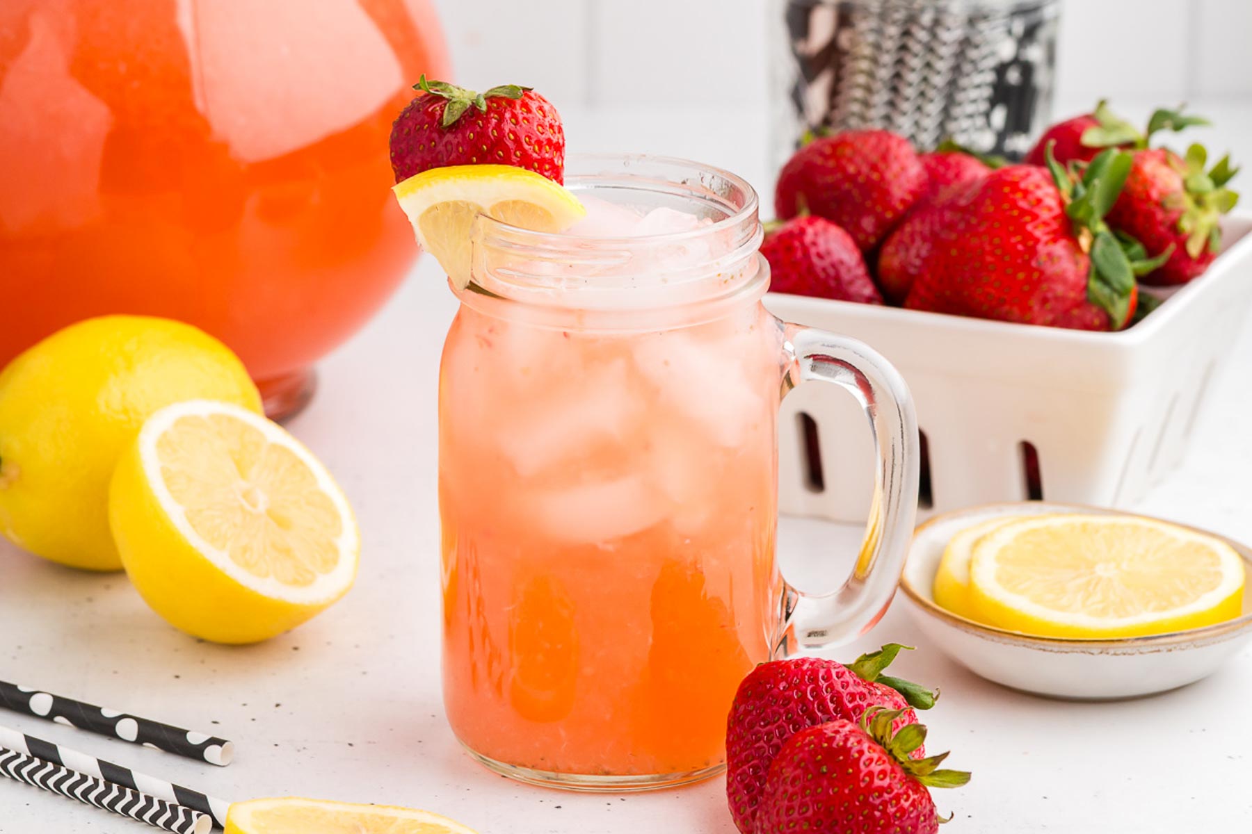 Easy Strawberry Lemonade in a glass with a pitcher and a pint of strawberries in the background