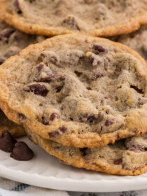 A close-up of a pile Eggless Chocolate Chip Cookies on a white plate.