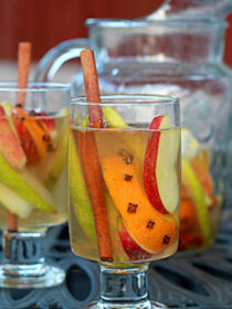 Clear glasses full of fall sangria with a pitcher of extra sangria in the background.