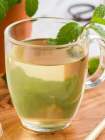 A mug of fresh mint tea on a wooden background with a gold spoon