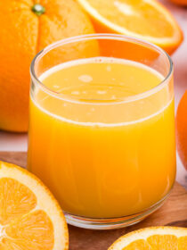 A clear glass full of orange juice with naval oranges all around
