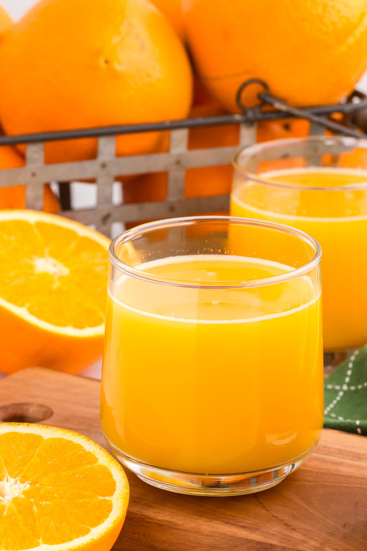 A clear glass of orange juice with a basket of oranges in the background