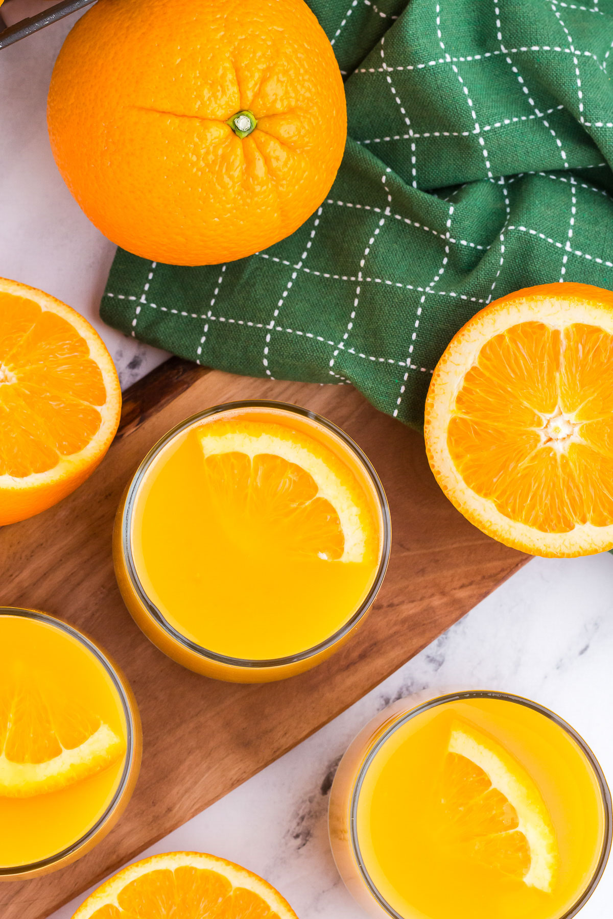 A top view of two glasses of orange juice with fresh orange slices for garnish. A green towel is in the background.