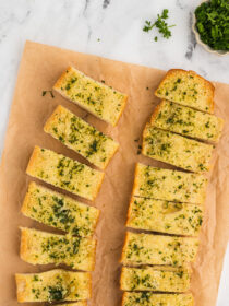 Slices of garlic herb bread on a wooden cutting board.