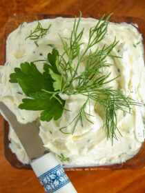 A wooden bowl with garlic herb cream cheese and a cheese knife.