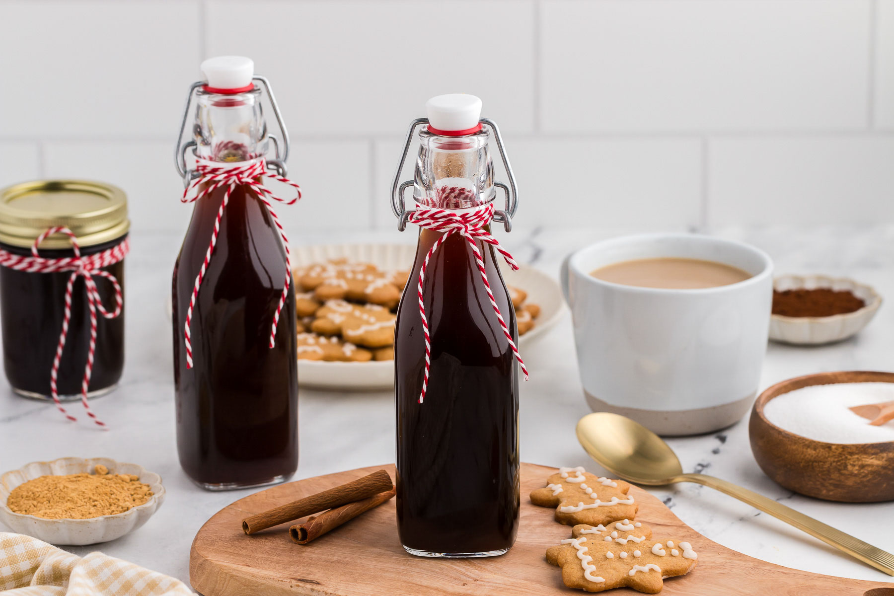 Two bottles of gingerbread coffee syrup with red and white twine and mini gingerbread cookies on a wooden board