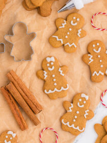 Mini gingerbread cookies on a wire rack with parchment paper and a piping bag and red baker's twine in the background.