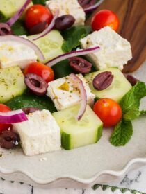 Close up of Greek Mosaic Salad on a white platter with a wooden spoon