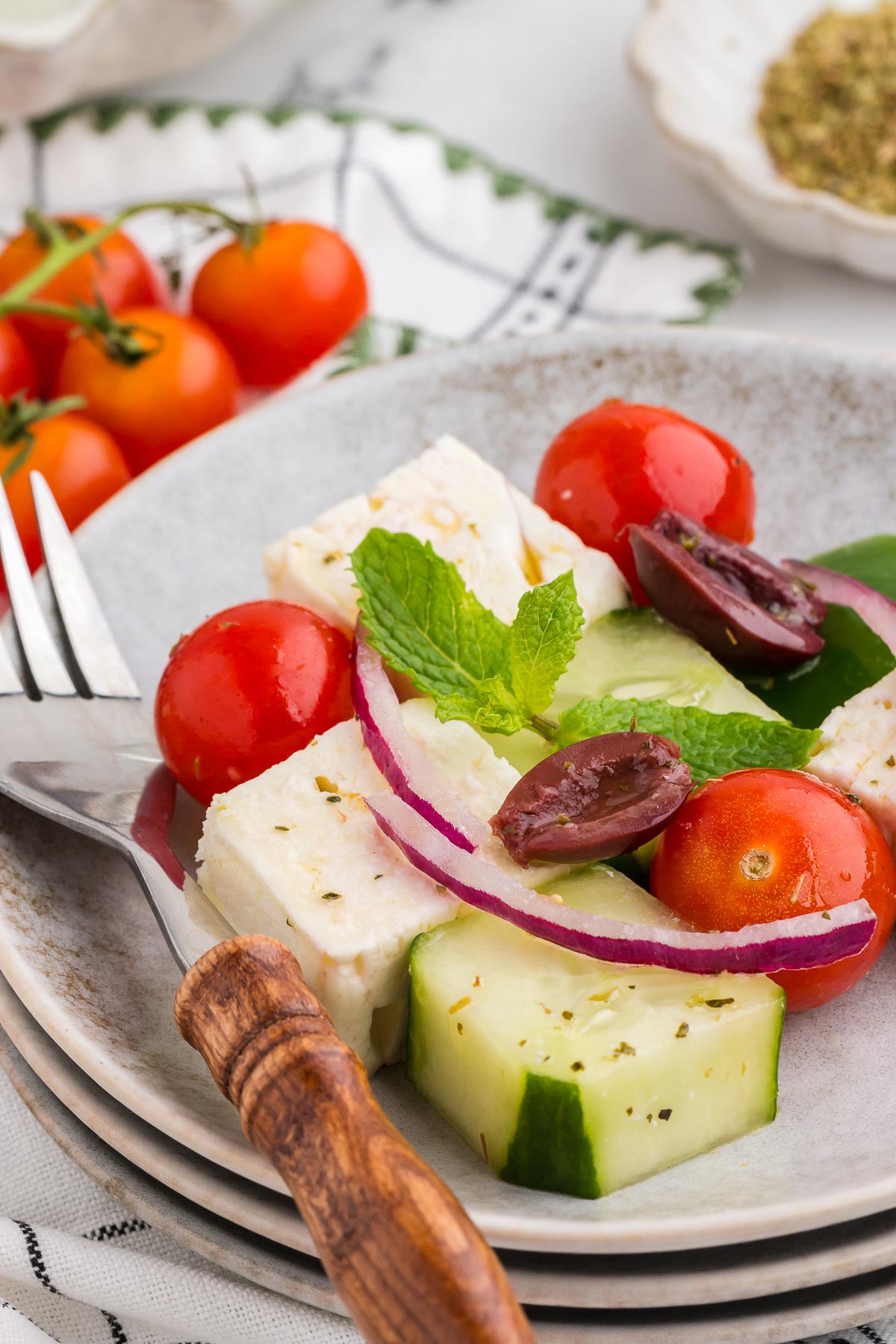 serving of greek mosaic salad on a stack of plates with a silver and wood fork