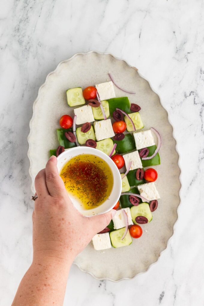 pouring the dressing over Greek Mosaic Salad
