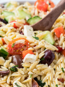 A spoon stirs Greek orzo salad.