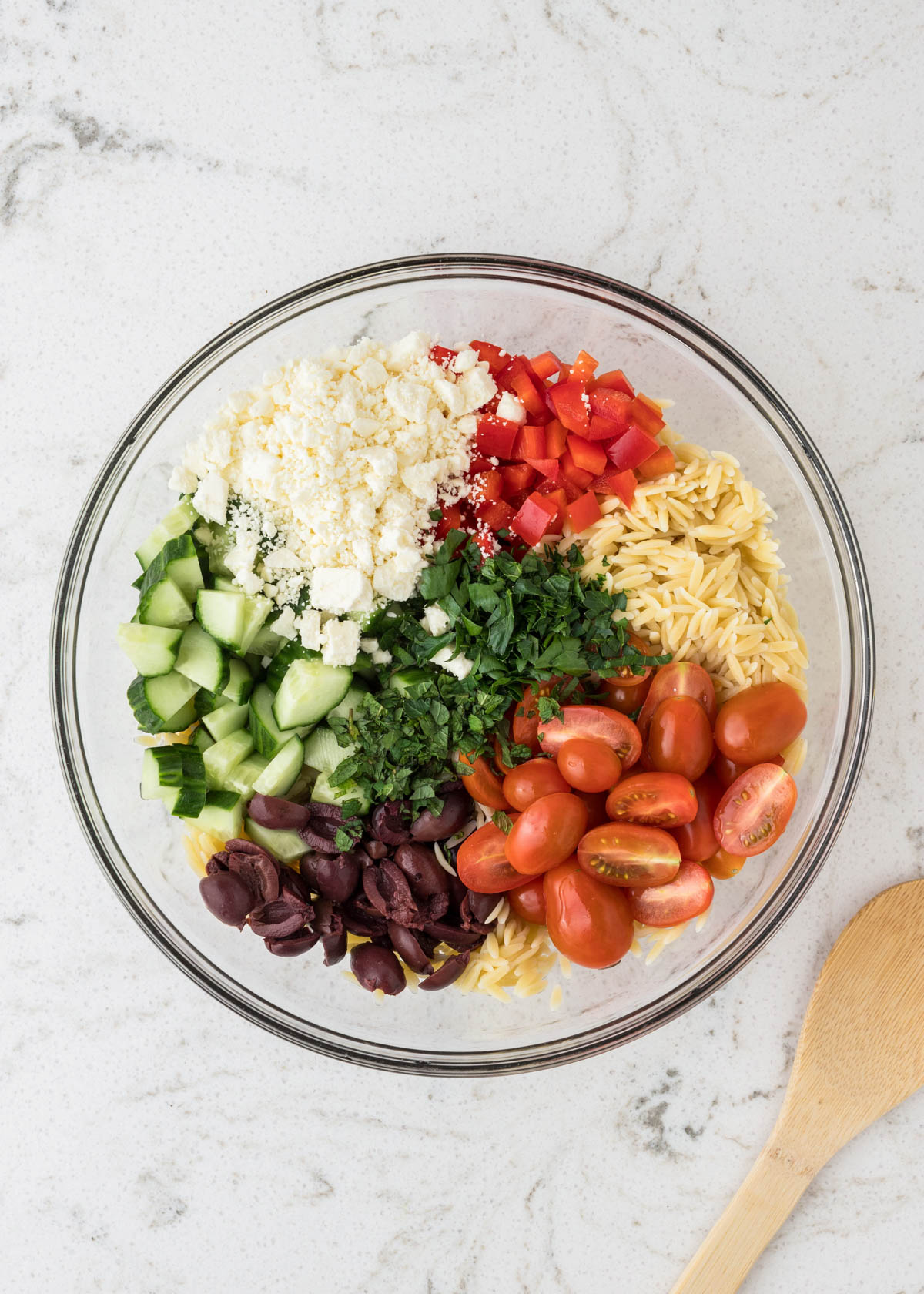 Ingredients for greek orzo pasta salad arranged in the salad bowl.