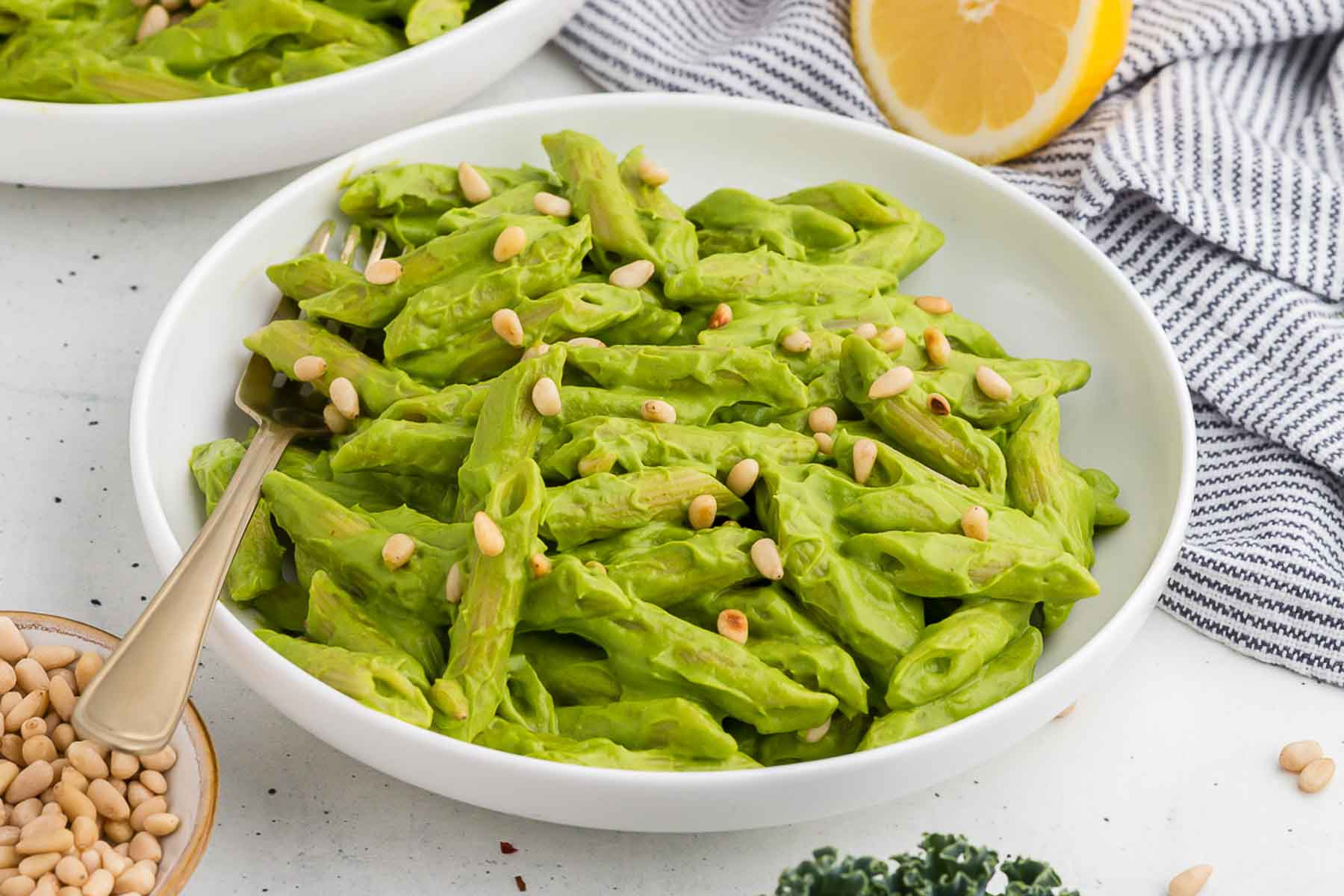 A white bowl full of avocado kale pesto pasta