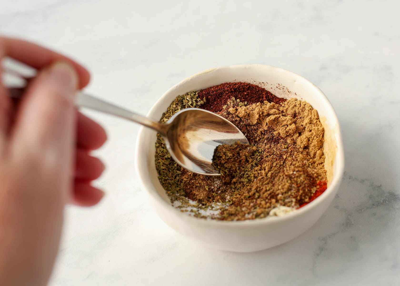 Spices for homemade taco seasoning being mixed up in a white bowl.