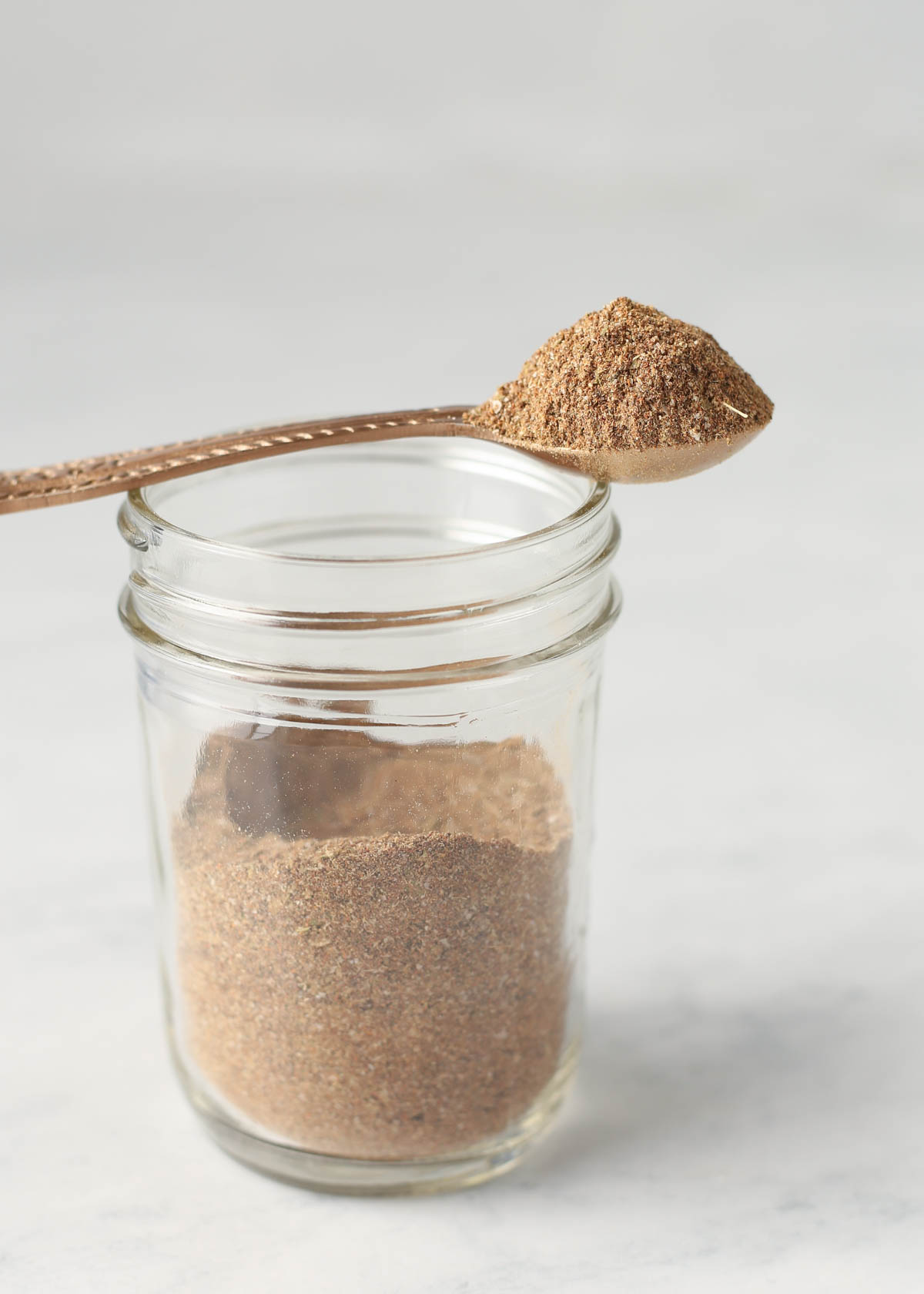 A jar of homemade taco seasoning with a measuring spoon on top of it.