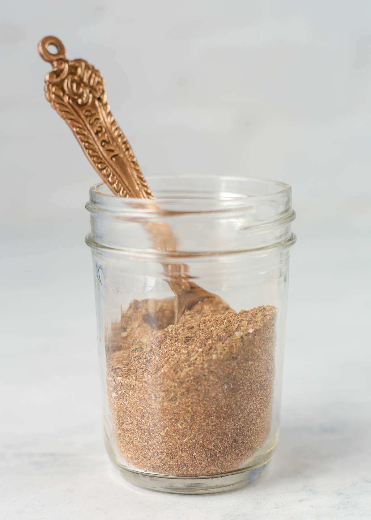 A jar of homemade taco seasoning with a measuring spoon inside it.