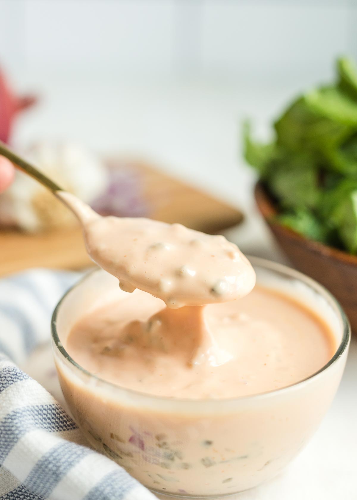 A spoonful of Thousand Island dressing in a glass bowl with a salad in the background.