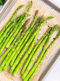 A tray of asparagus is prepped for roasting in the oven. It is on a piece of parchment paper on a silver rimmed baking sheet.