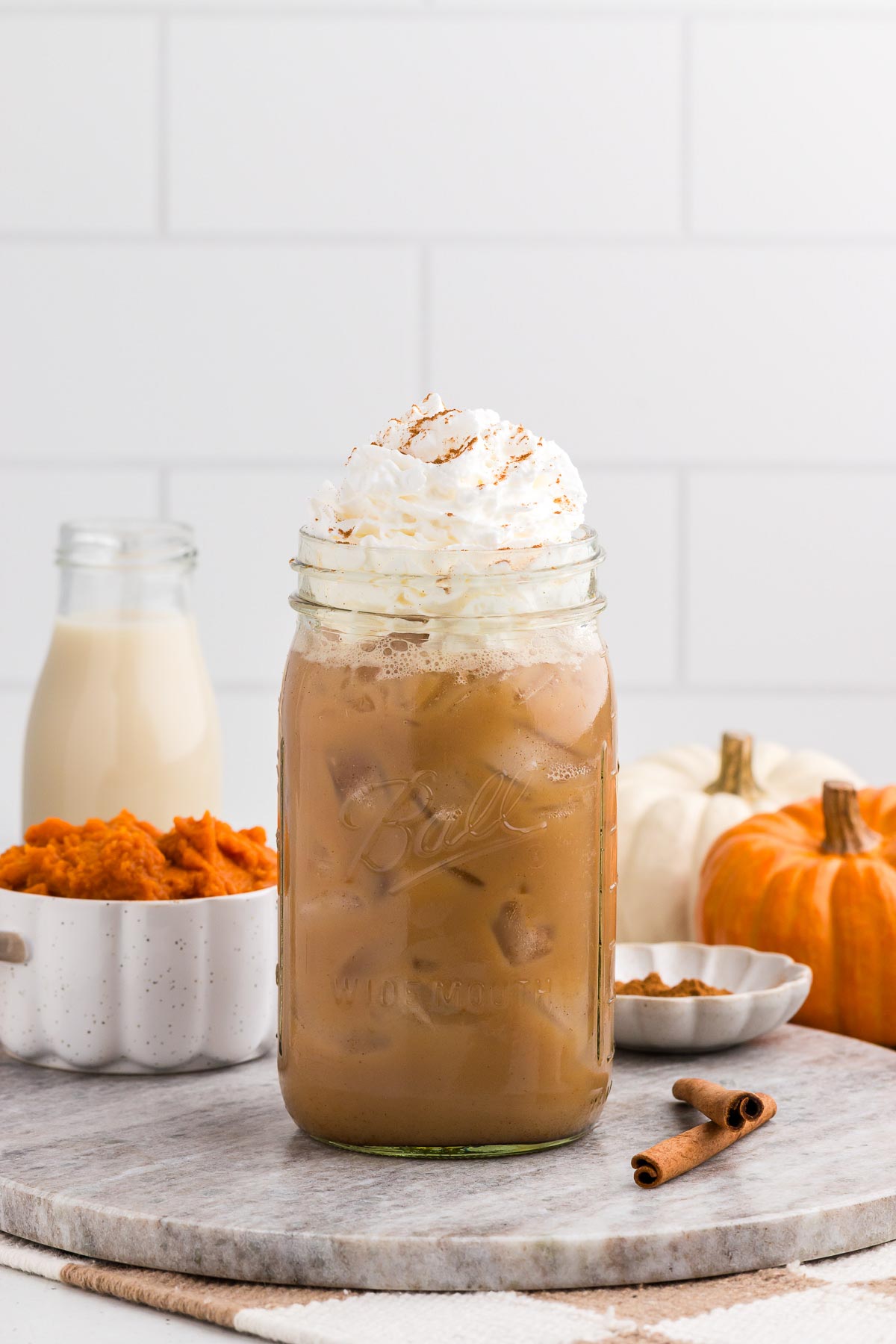 iced pumpkin spice latte with pumpkin and puree in the background and a cinnamon stick alongside