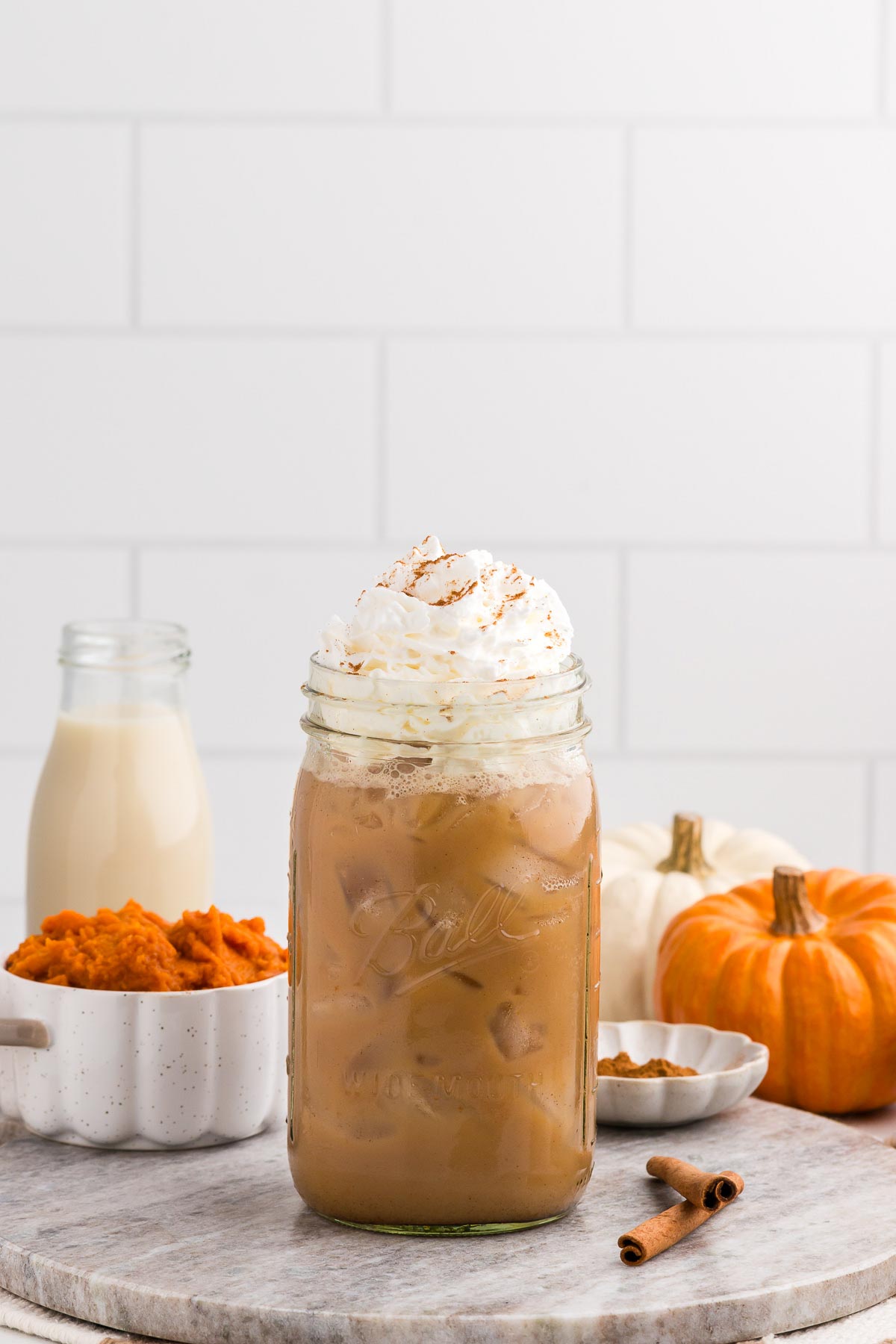 iced pumpkin spice latte with pumpkin and puree in the background and a cinnamon stick alongside