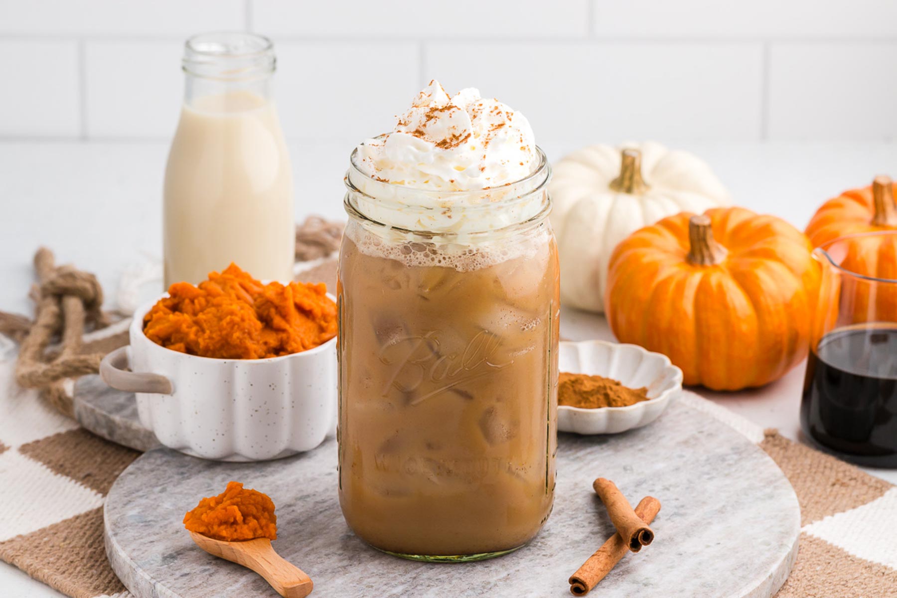 iced pumpkin spice latte with pumpkin and puree in the background and a cinnamon stick alongside