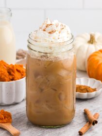 iced pumpkin spice latte with pumpkin and puree in the background and a cinnamon stick alongside