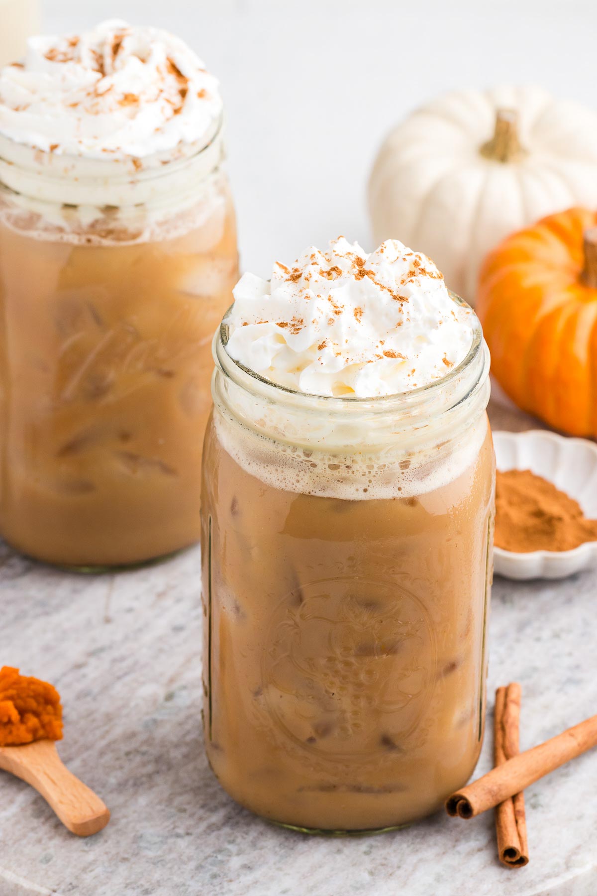Iced Pumpkin Spiced Latte in mason jars with cinnamon and pumpkin in the background