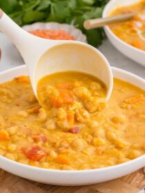 Instant Pot Coconut Red Lentil Soup in a white bowl with a ladle adding more soup to the bowl