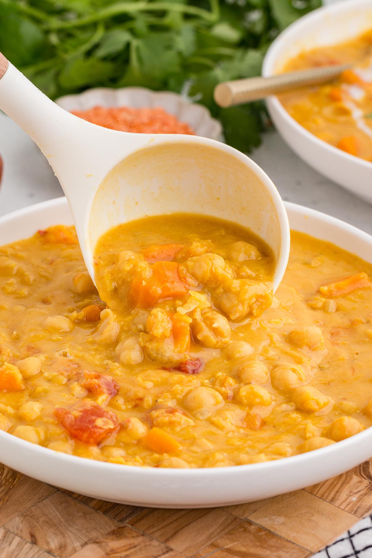 Instant Pot Coconut Red Lentil Soup in a white bowl with a ladle adding more soup to the bowl