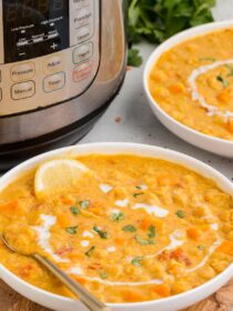 Instant Pot Coconut Red Lentil Soup in a white bowl with a lemon slice and cilantro for garnish. An Instant Pot is in the background.