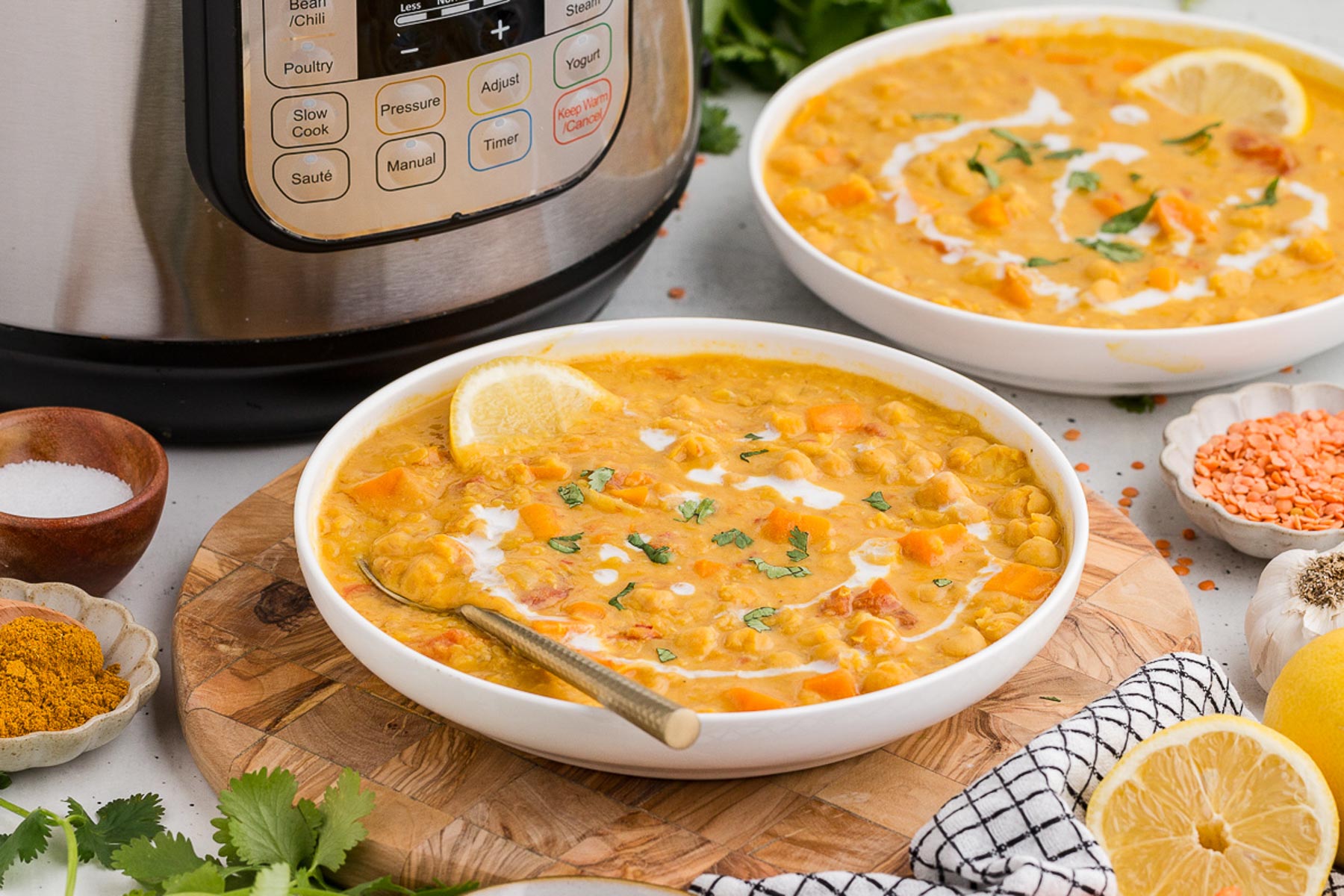 Instant Pot Coconut Red Lentil Soup in a white bowl with a lemon slice and cilantro for garnish. An Instant Pot is in the background.
