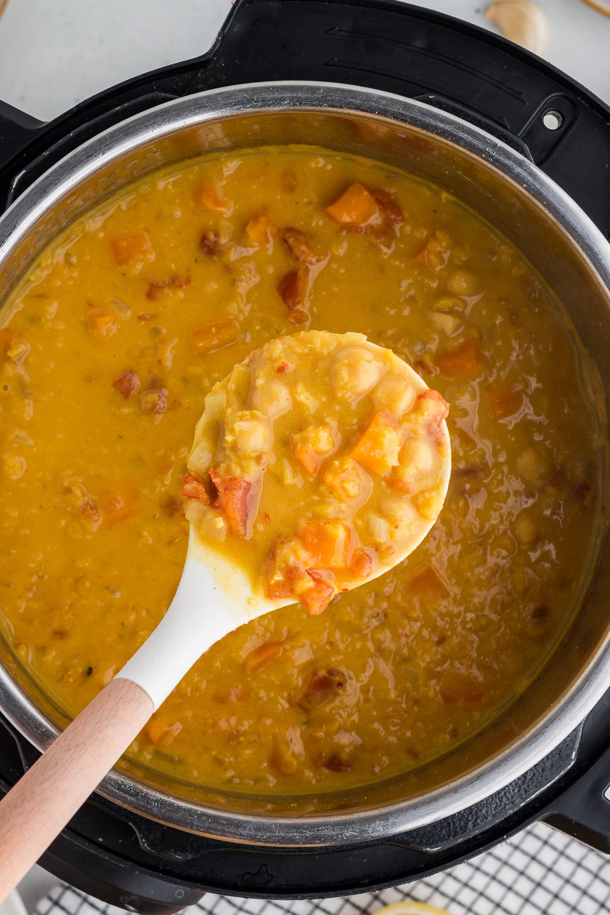 Instant Pot Coconut Red Lentil Soup in the Instant Pot with a white and wood ladle lifting out some of the soup