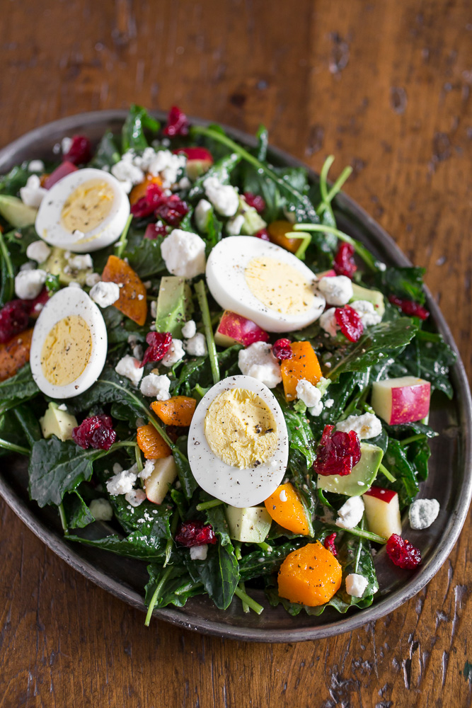 A large bowl of winter kale salad topped with eggs, blue cheese, and apples. 