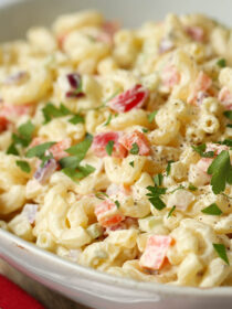 macaroni salad with parsley garnish in a white bowl with a red napkin in the background