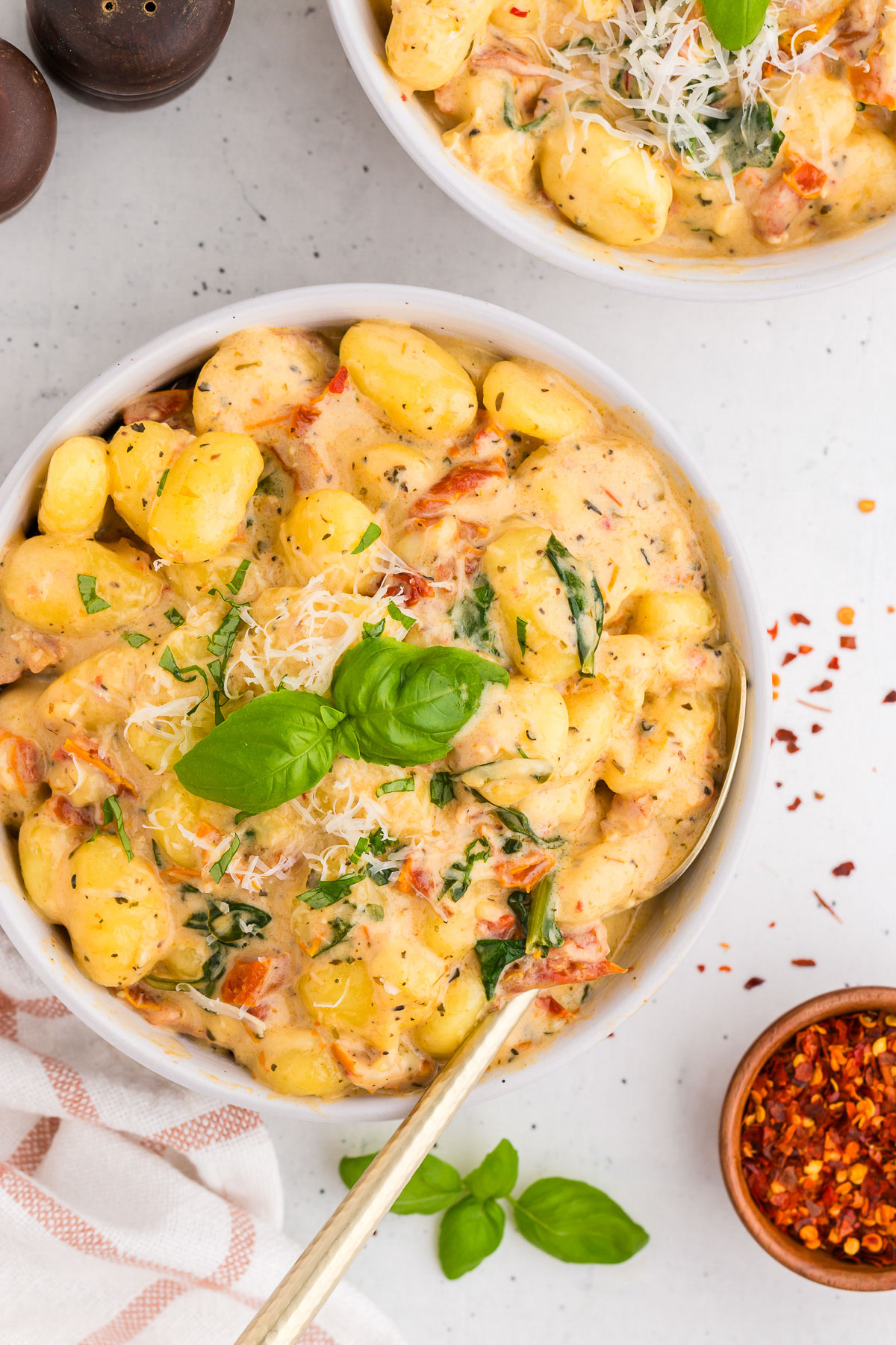 Top view of creamy Tuscan marry-me gnocchi in a white bowl with a gold spoon. A garnish of basil is on top.