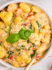 Top view of creamy Tuscan marry-me gnocchi in a white bowl with a gold spoon. A garnish of basil is on top.