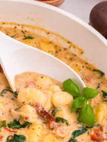 Creamy marry-me gnocchi in a saute pan with a white spoon scooping some out.