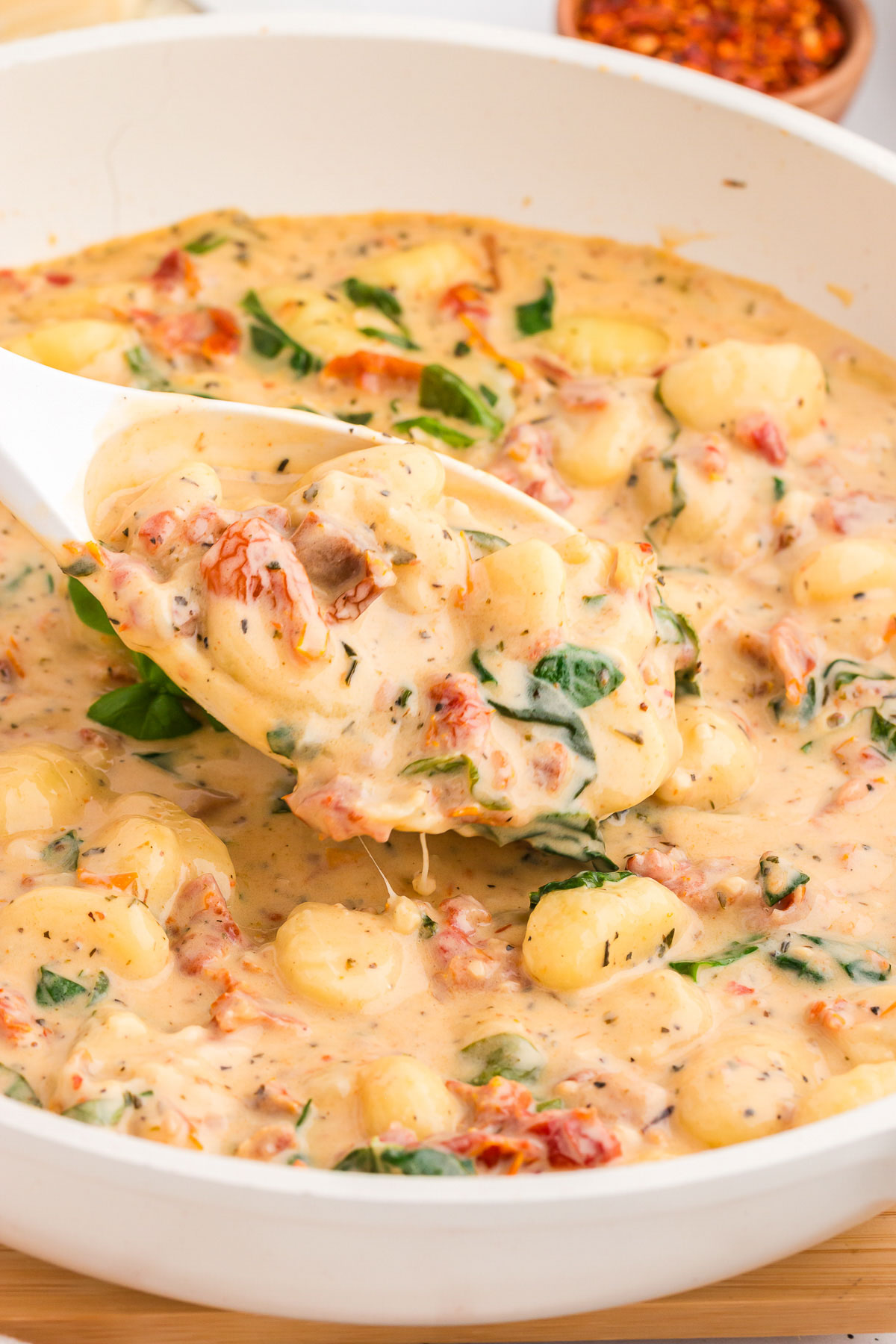 Creamy marry-me gnocchi in a saute pan with a white spoon scooping some out.