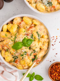 Top view of creamy Tuscan marry-me gnocchi in a white bowl with a gold spoon. A garnish of basil is on top.