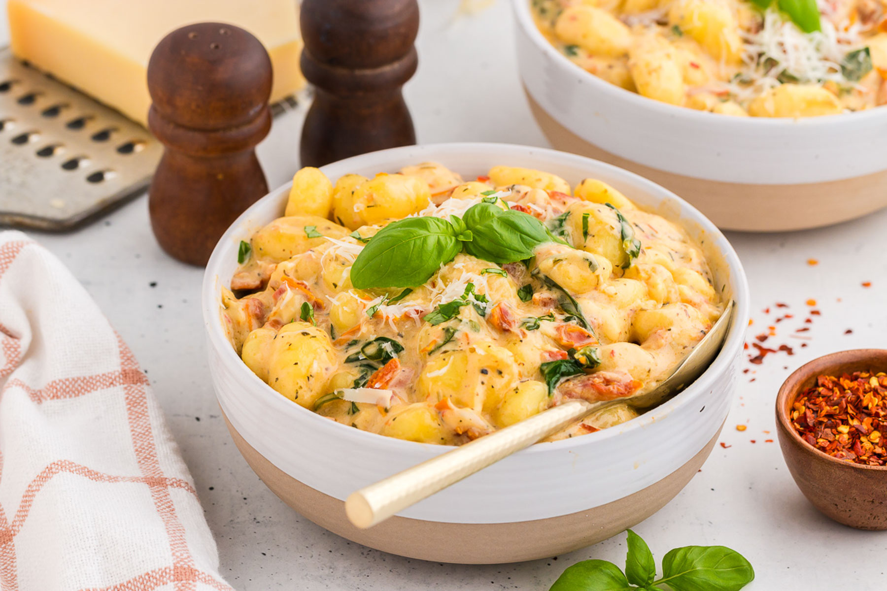 A bowl of marry-me gnocchi in a white bowl with dark wood salt and pepper shakers. A gold spoon is in the bowl.