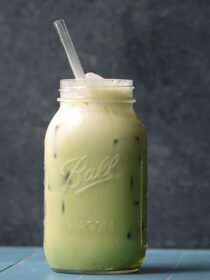 An iced matcha latte with a straw in it on a blue table.