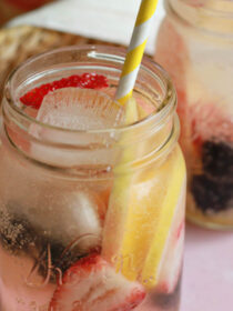 Sangria by the jar served with a yellow straw on a pink background.