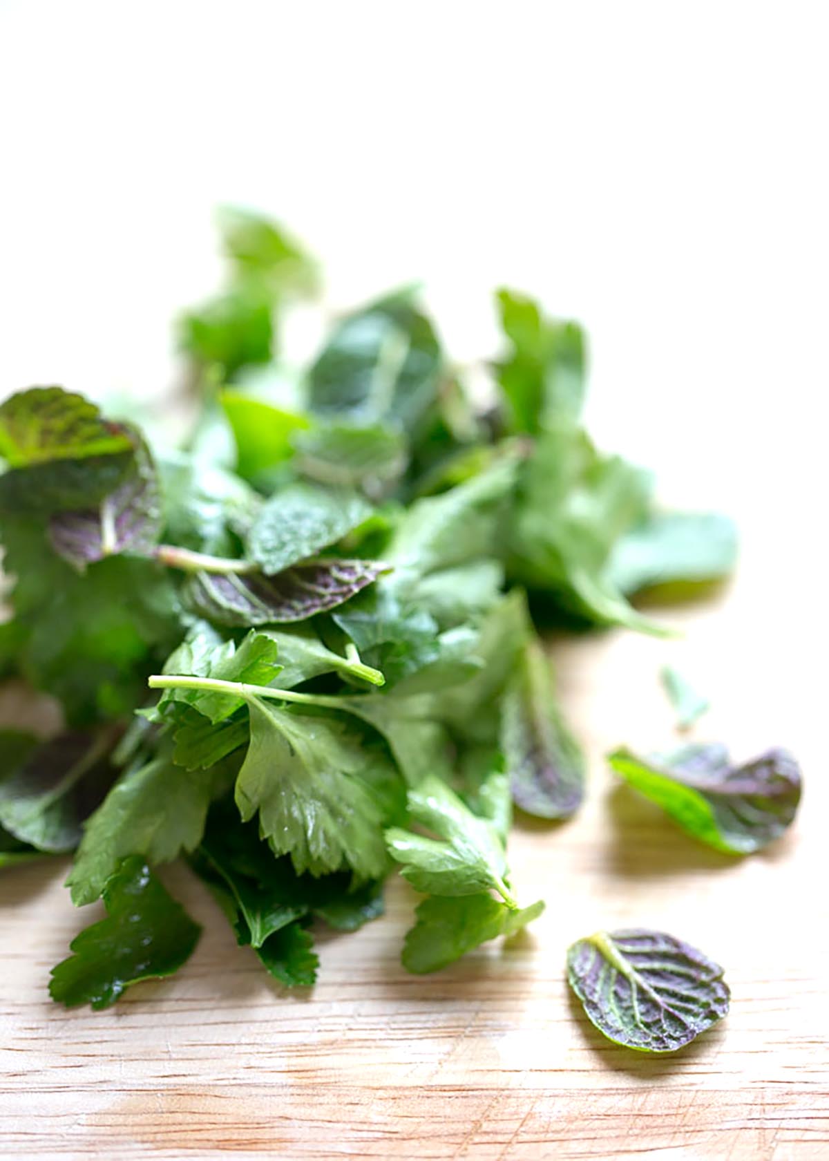 Parsley and mint leaves on a bamboo cutting board, ready to chop for gremolata. 