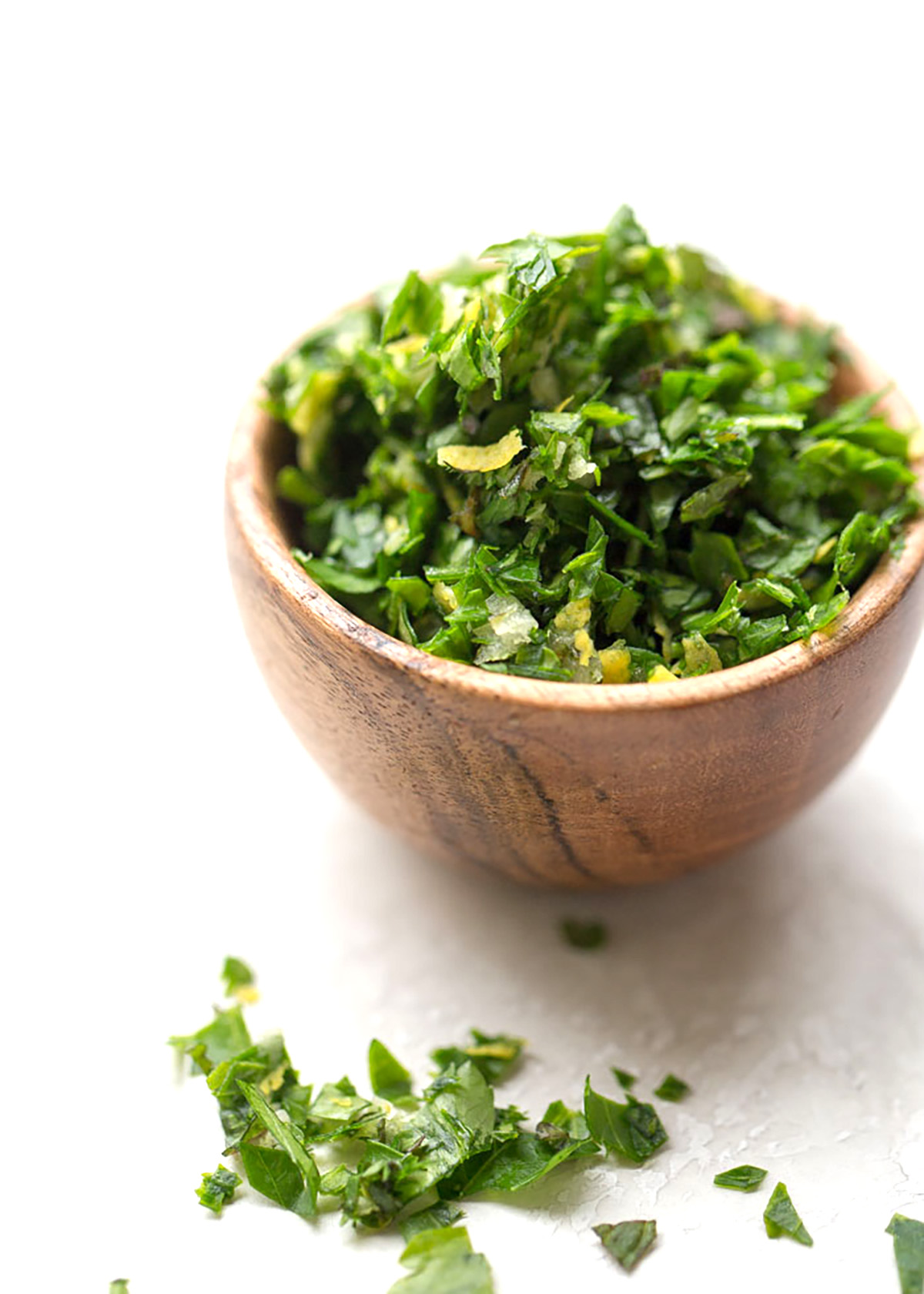 Tiny wooden bowl full of mint gremolata on a white plaster background, with some more gremolata in the foreground. 