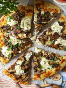 A top view of mushroom pizza with a slice pulled out. An orange and beige striped napkin is in the background, with a candle and parsley.