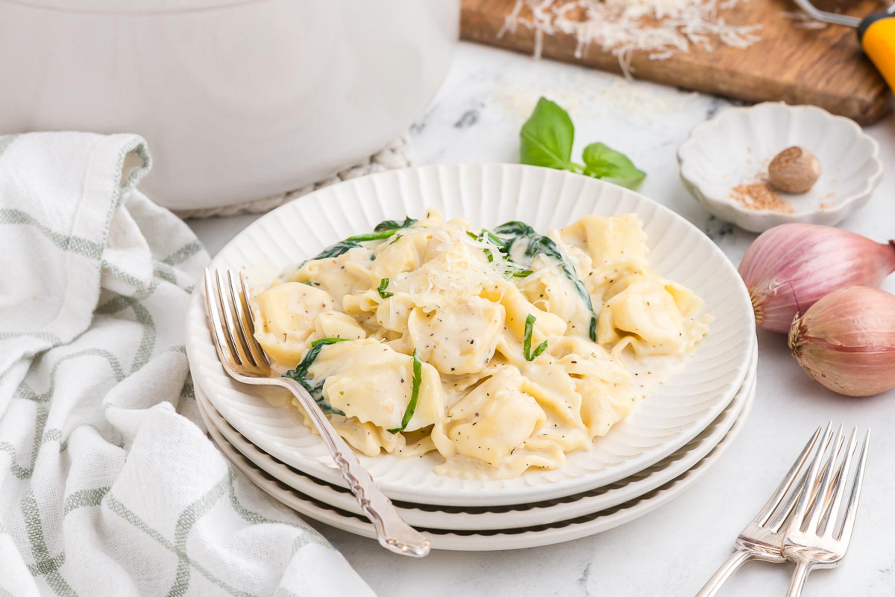 a serving of creamy one-pot tortellini Alfredo on a stack of white plates with silver forks